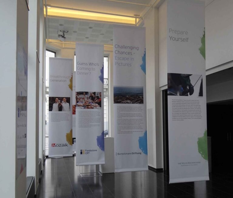 Impression sur toile blanche suspendue depuis le plafond avec du texte et des photos créant un parcours pour le visiteur dans une expositions.