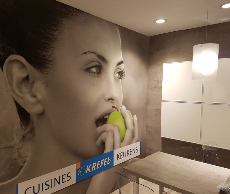 Toile murale en une seule pièce imprimée en grand format par Casprint, représentant une femme mangeant une pomme, installée dans un espace intérieur moderne pour le salon Batibouw