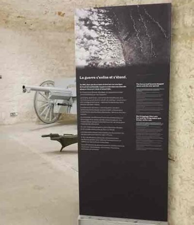 Impression vinyle autocollant repositionnable - Affiche promotionnelle grand format - Pose facile sans bulles Panneau d'information vertical en vinyle imprimé avec texte bilingue et photo, installé dans un espace au Musée de Pompelle à Metz près d'une pièce d'artillerie.