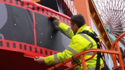 Pose de vinyle imprimé avec un motif rouge et noir rappelant une bobine de film sur façade d'attraction par professionnel en hauteur