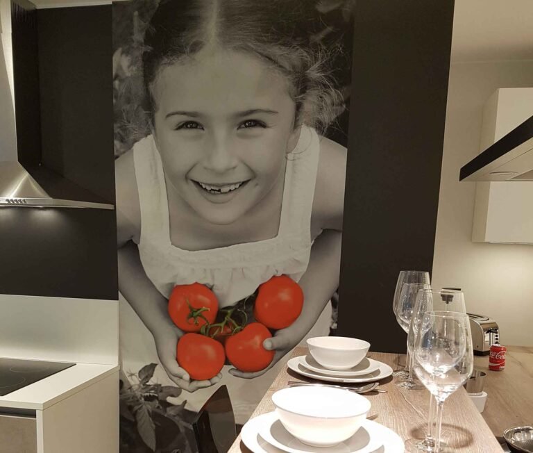 Toile murale en une seule pièce imprimée en grand format par Casprint, représentant une petite fille tenant des tomates dans les mains, installée dans une cuisine moderne pour le salon Batibouw Krefel