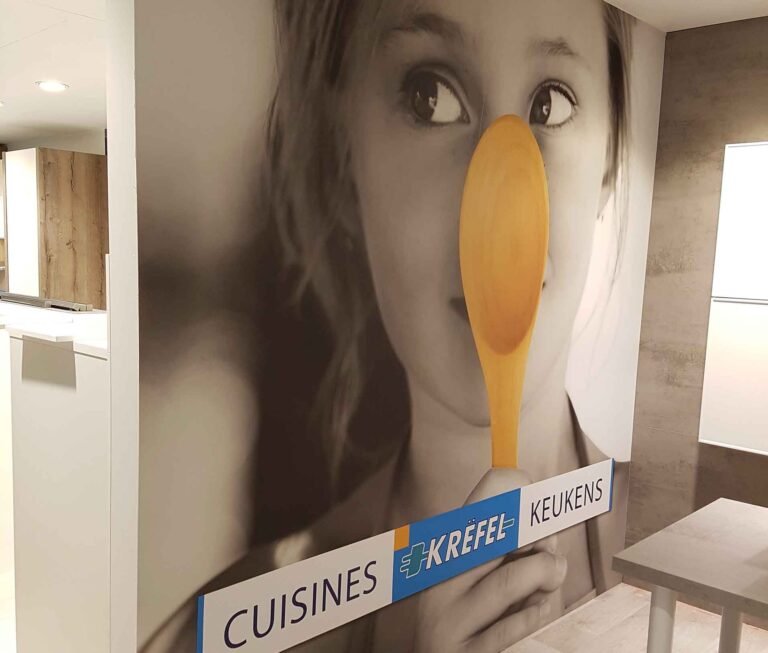 Toile murale en une seule pièce imprimée en grand format par Casprint, représentant une petite fille tenant cuillère en bois devant son nez, installée dans une un espace d'acceuil moderne pour le salon Batibouw Krefel