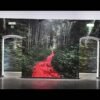 Mur imprimé en grand format sur papier Blueback montrant une forêt dense avec un tapis rouge s’étendant au centre, installé dans une exposition.