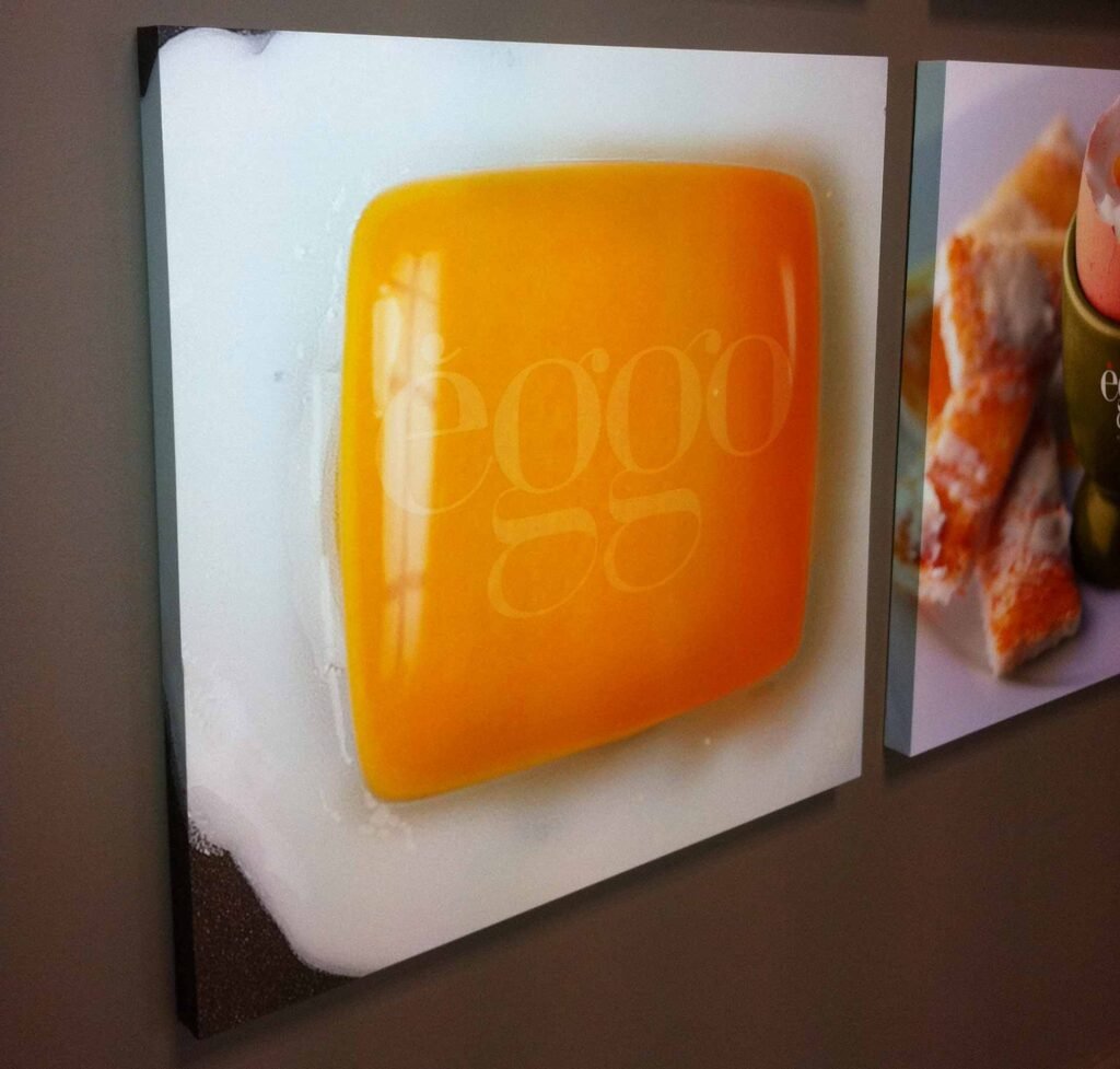 Toile imprimée sur cadre exposée au salon Batibouw, présentant un gros plan artistique d’un jaune d’œuf carré dans du blanc d’œuf.