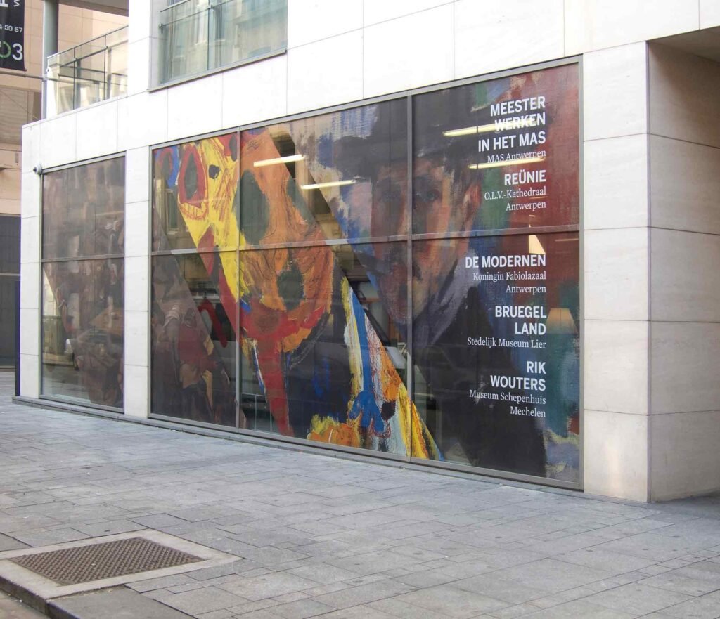 Vitrophanie One-Way Vision imprimée avec une affiche pour une exposition d'art dans un musée les tons jaune orangé sur vitrine, visibilité extérieure et transparence intérieure.